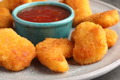 Photo of Plate with hot chili sauce and nuggets on grey table, closeup