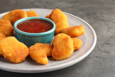 Photo of Plate with hot chili sauce and nuggets on grey textured table, closeup