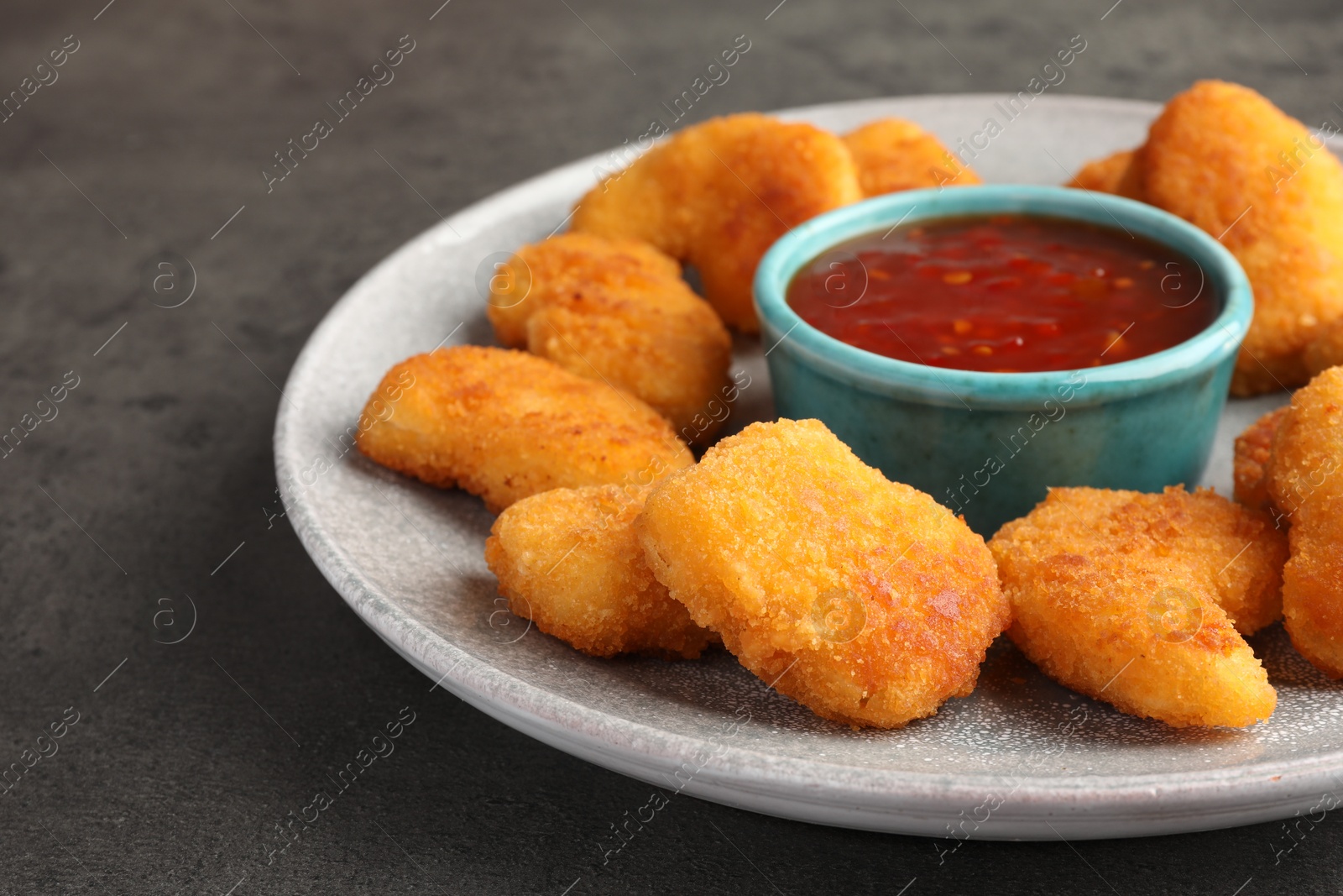 Photo of Plate with hot chili sauce and nuggets on grey textured table, closeup