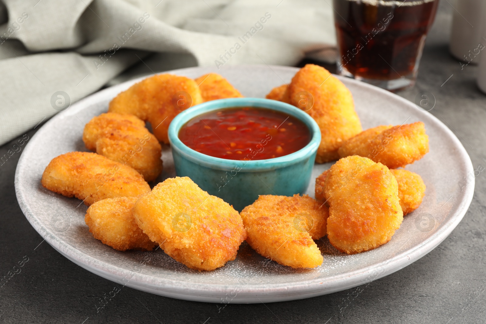 Photo of Plate with hot chili sauce and nuggets on grey textured table, closeup