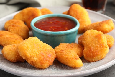 Photo of Plate with hot chili sauce and nuggets on grey table, closeup