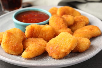 Photo of Plate with hot chili sauce and nuggets on grey table, closeup