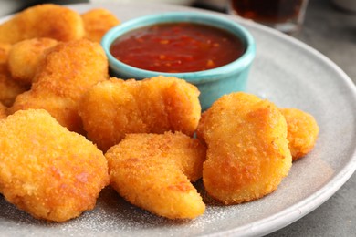 Photo of Plate with hot chili sauce and nuggets on grey table, closeup