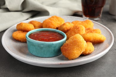 Photo of Plate with hot chili sauce and nuggets on grey textured table, closeup