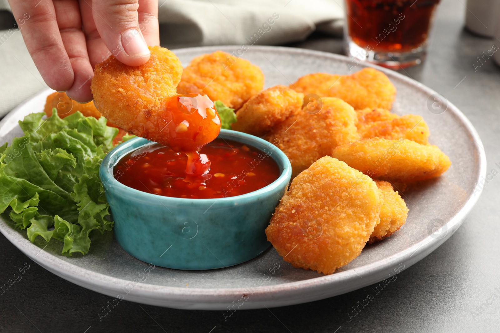 Photo of Woman dipping nugget into chili sauce at grey table, closeup