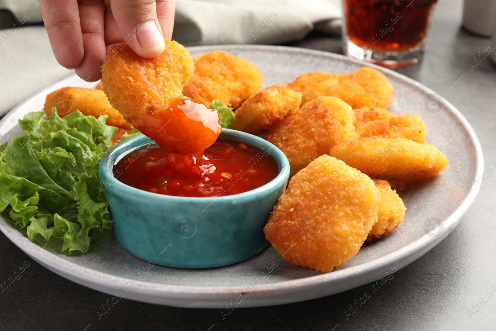 Photo of Woman dipping nugget into chili sauce at grey table, closeup