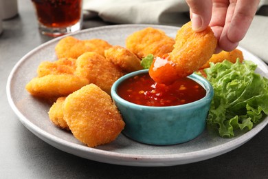 Photo of Woman dipping nugget into chili sauce at grey table, closeup