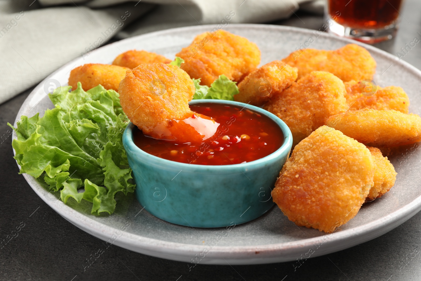 Photo of Plate with hot chili sauce, lettuce and nuggets on grey table, closeup