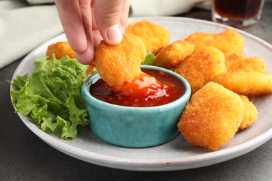 Photo of Woman dipping nugget into chili sauce at grey table, closeup