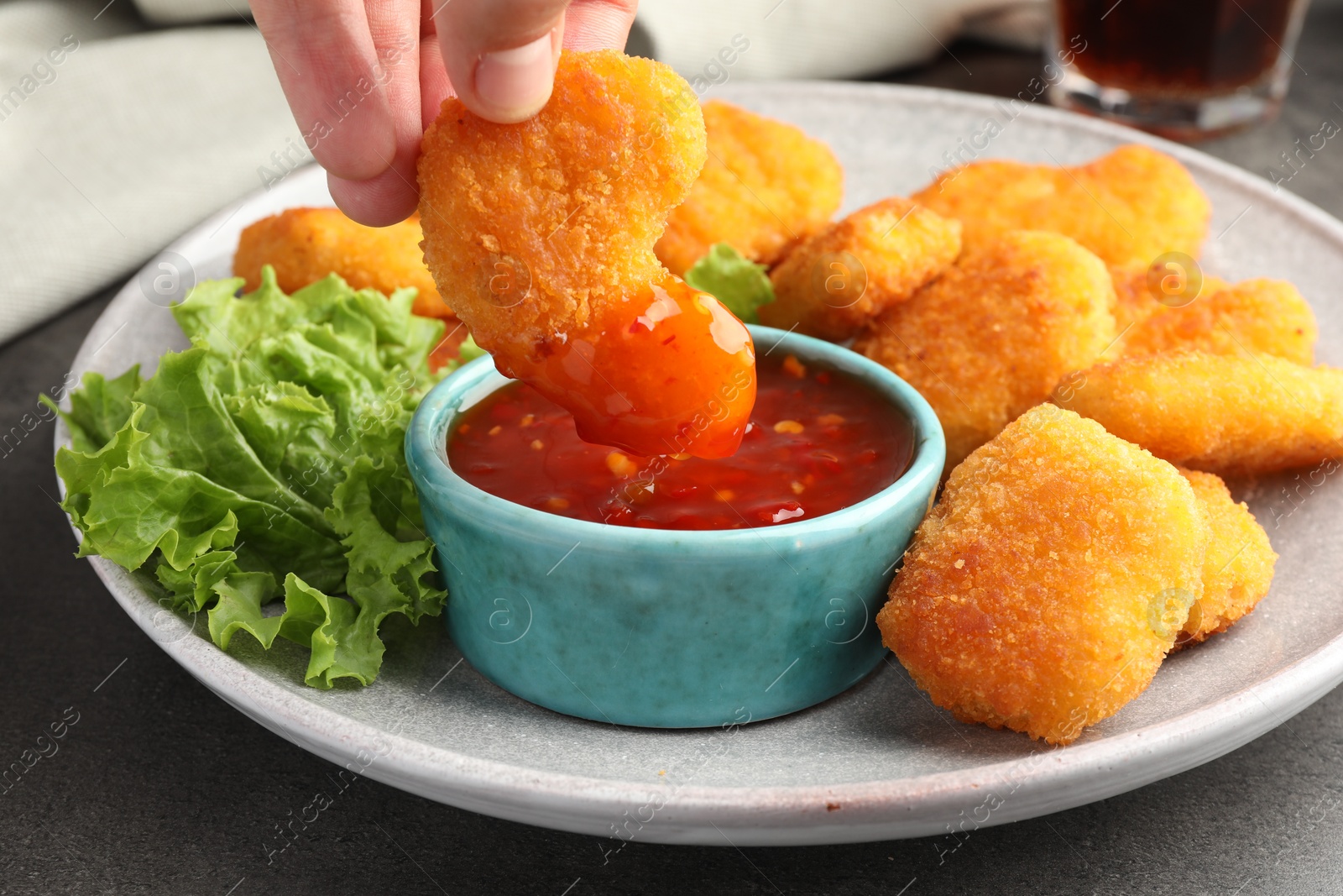 Photo of Woman dipping nugget into chili sauce at grey table, closeup