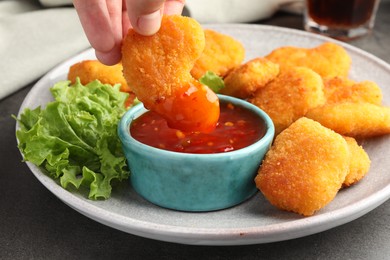 Photo of Woman dipping nugget into chili sauce at grey table, closeup