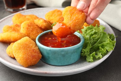 Photo of Woman dipping nugget into chili sauce at grey table, closeup