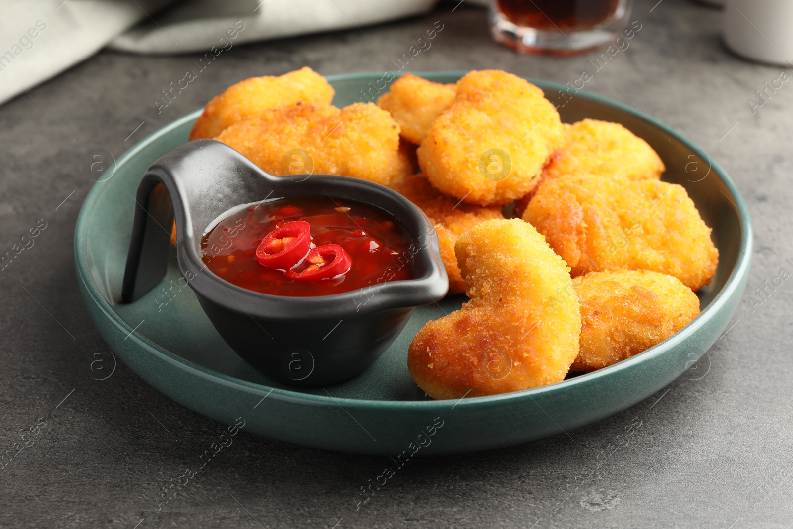 Photo of Plate with hot chili sauce and nuggets on grey textured table, closeup