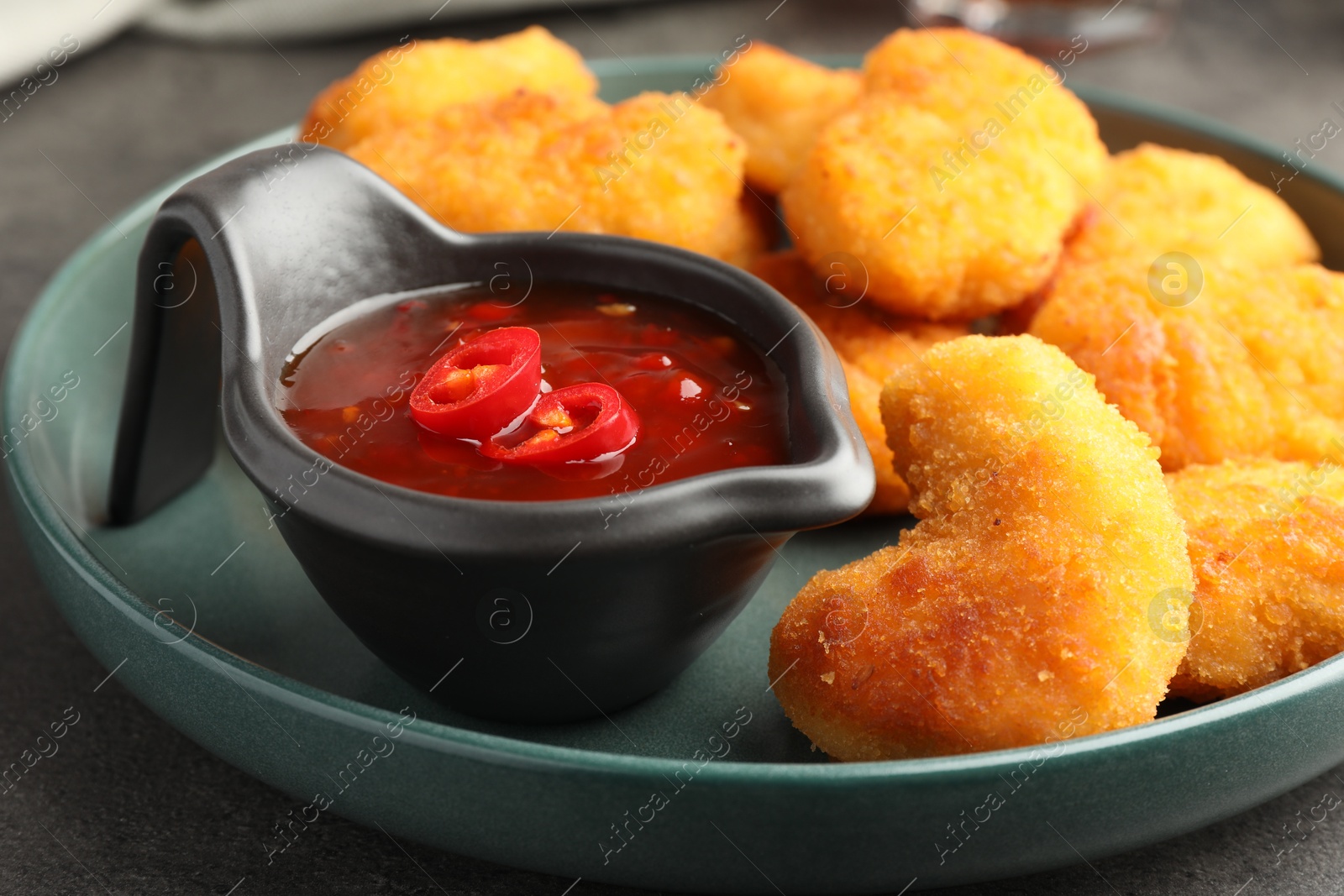 Photo of Plate with hot chili sauce and nuggets on grey table, closeup