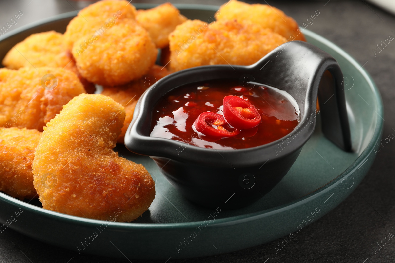 Photo of Plate with hot chili sauce and nuggets on grey table, closeup