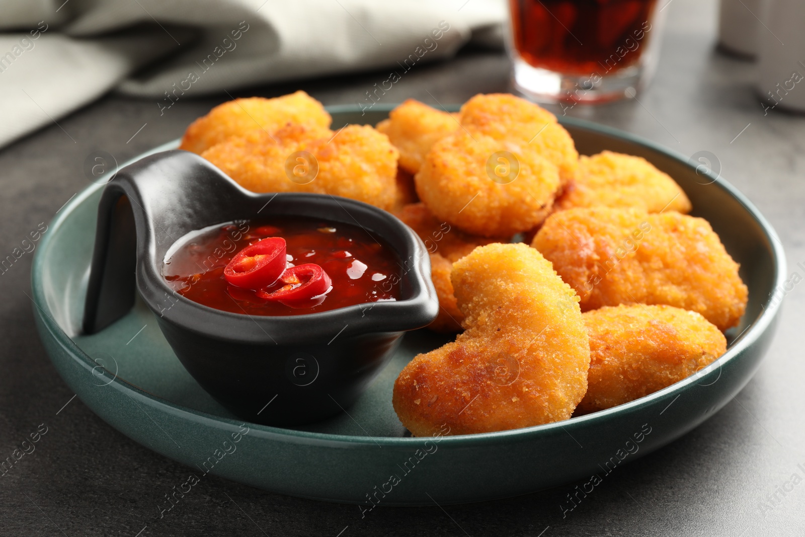 Photo of Plate with hot chili sauce and nuggets on grey table, closeup