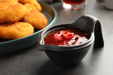 Photo of Hot chili sauce in gravy boat on grey textured table, closeup