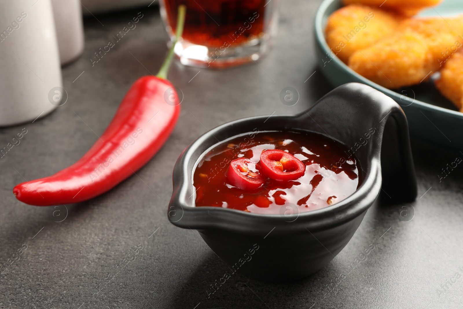 Photo of Hot chili sauce in gravy boat on grey textured table, closeup