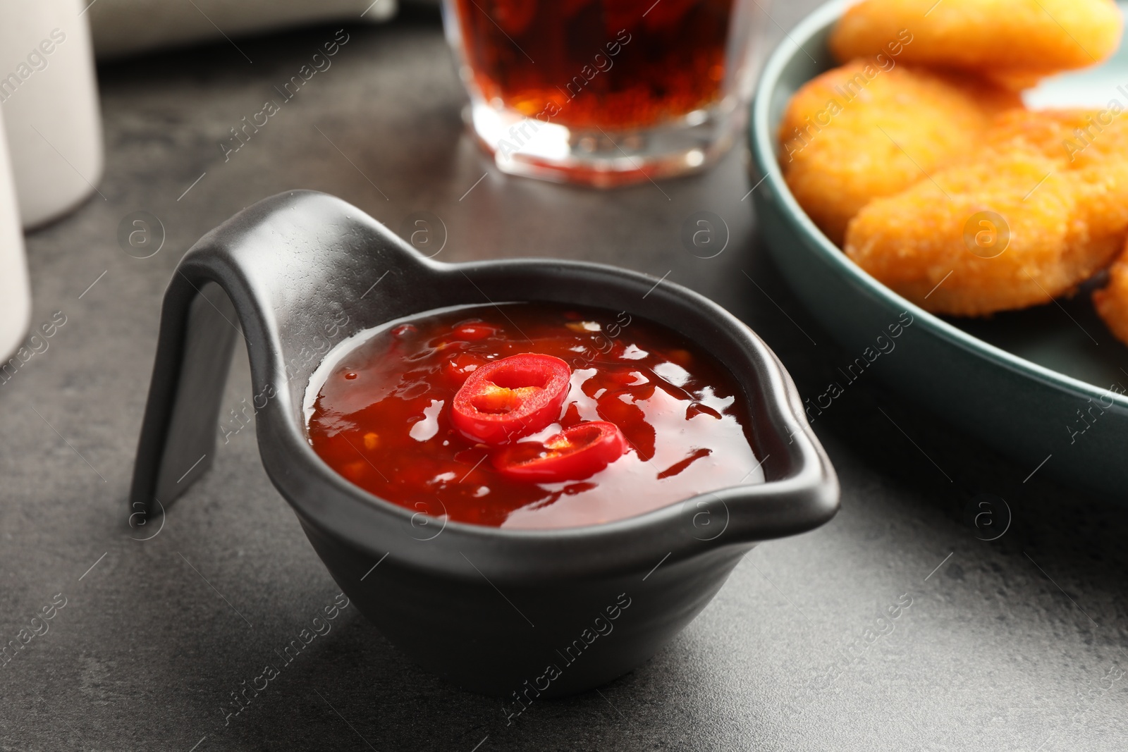 Photo of Hot chili sauce in gravy boat on grey textured table, closeup