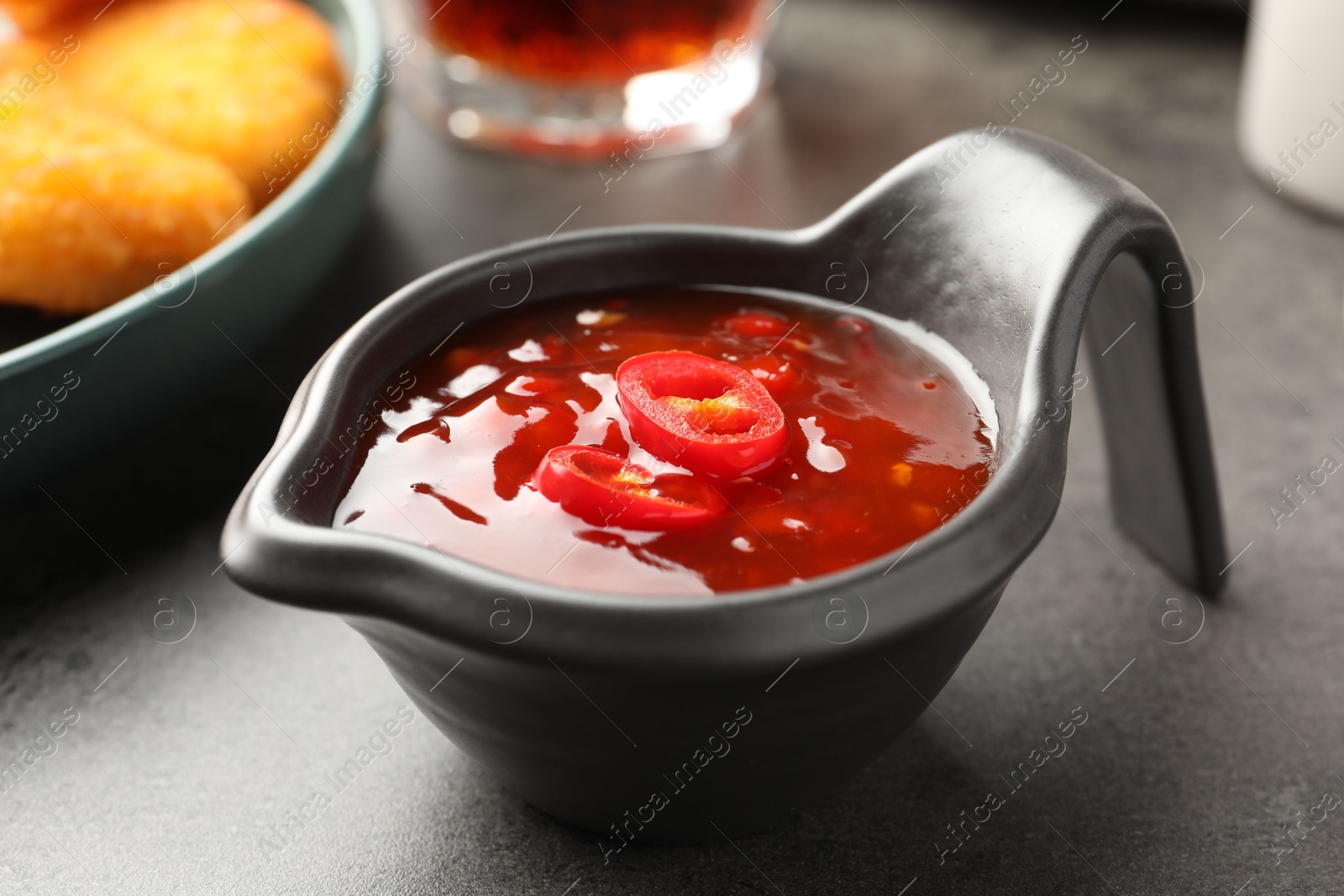 Photo of Hot chili sauce in gravy boat on grey textured table, closeup