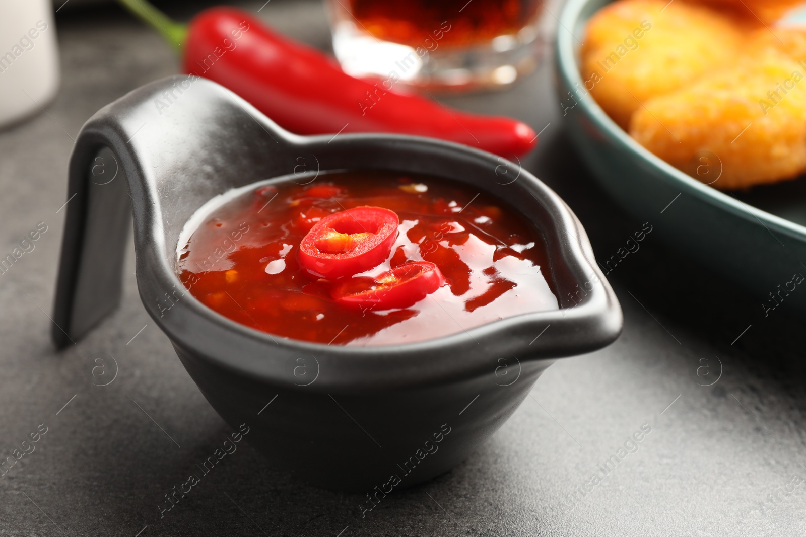 Photo of Hot chili sauce in gravy boat on grey textured table, closeup