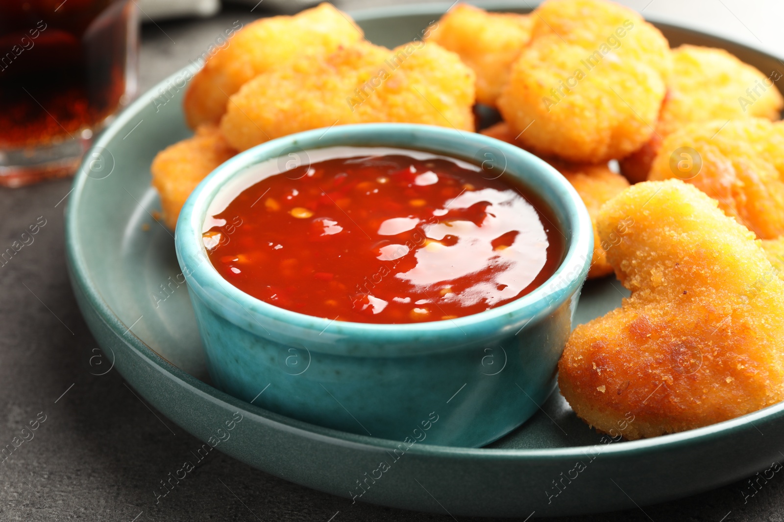 Photo of Plate with hot chili sauce and nuggets on grey textured table, closeup