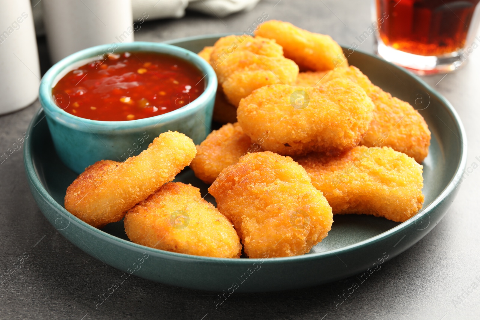 Photo of Plate with hot chili sauce and nuggets on grey textured table, closeup