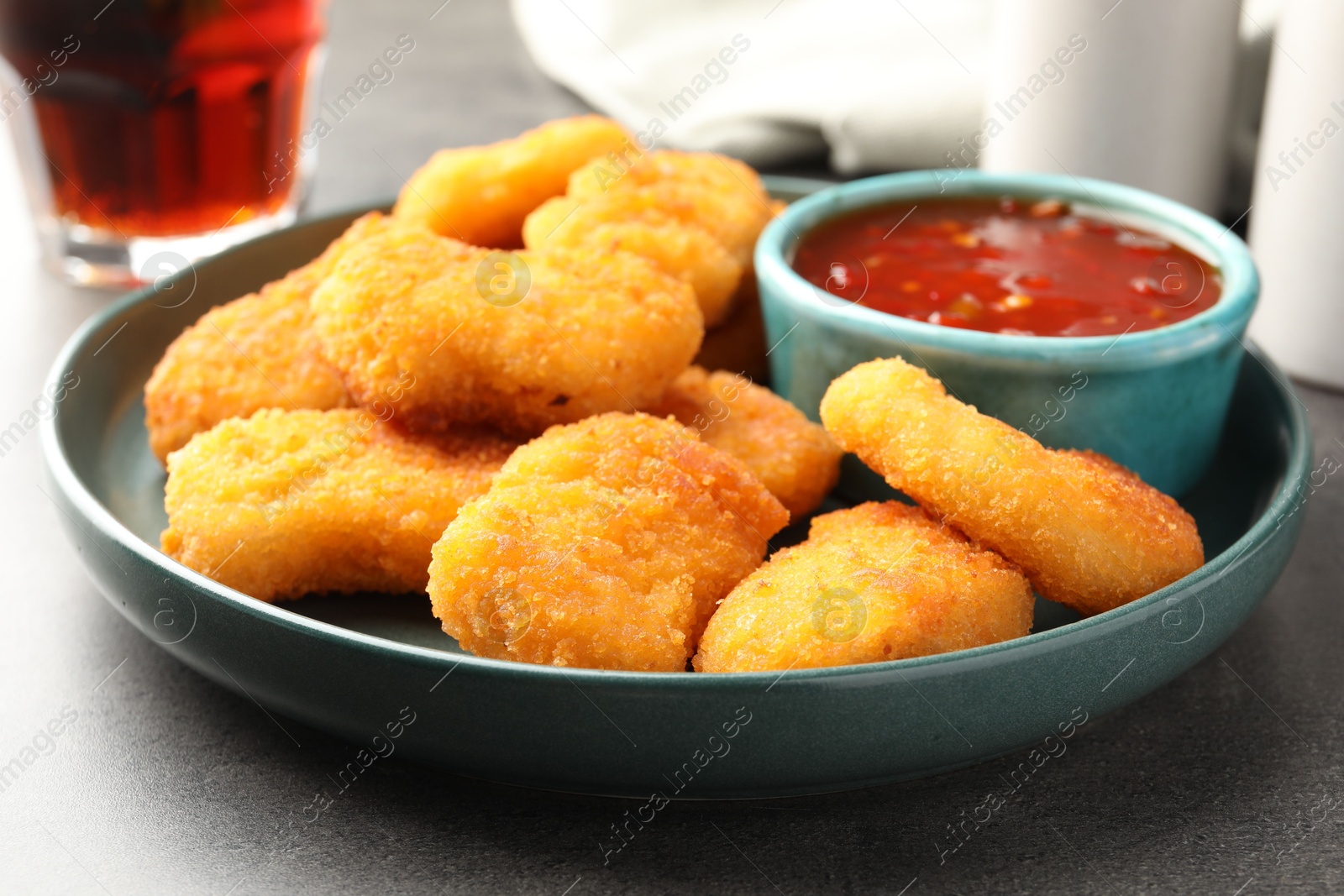 Photo of Plate with hot chili sauce and nuggets on grey textured table, closeup