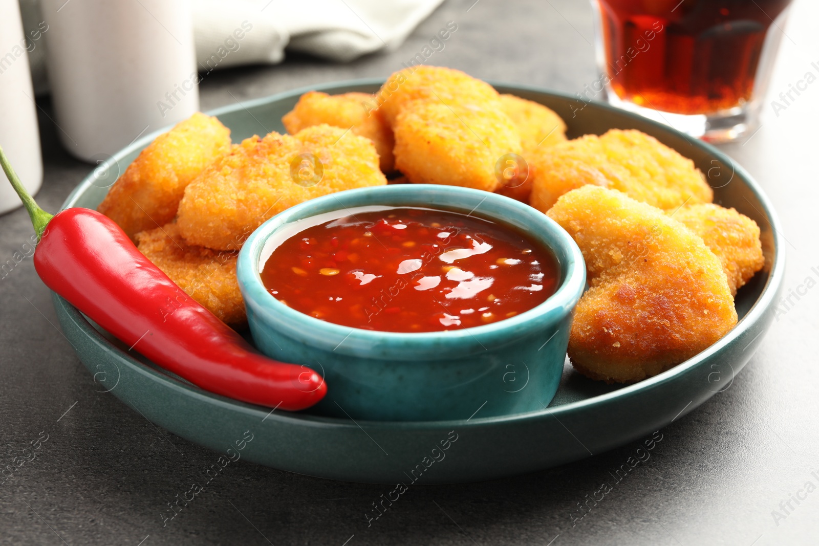 Photo of Plate with hot chili sauce, pepper and nuggets on grey textured table, closeup