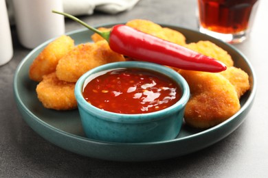 Photo of Plate with hot chili sauce, pepper and nuggets on grey textured table, closeup