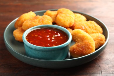 Photo of Plate with hot chili sauce and nuggets on wooden table, closeup