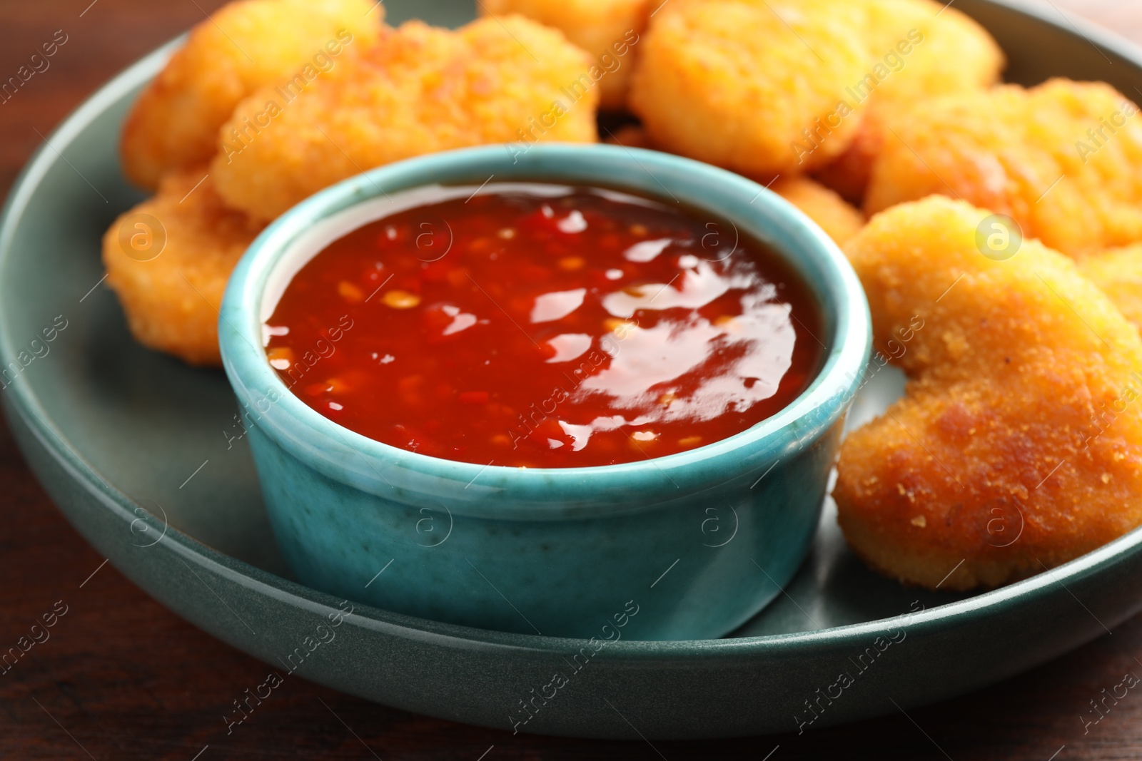 Photo of Plate with hot chili sauce and nuggets on wooden table, closeup