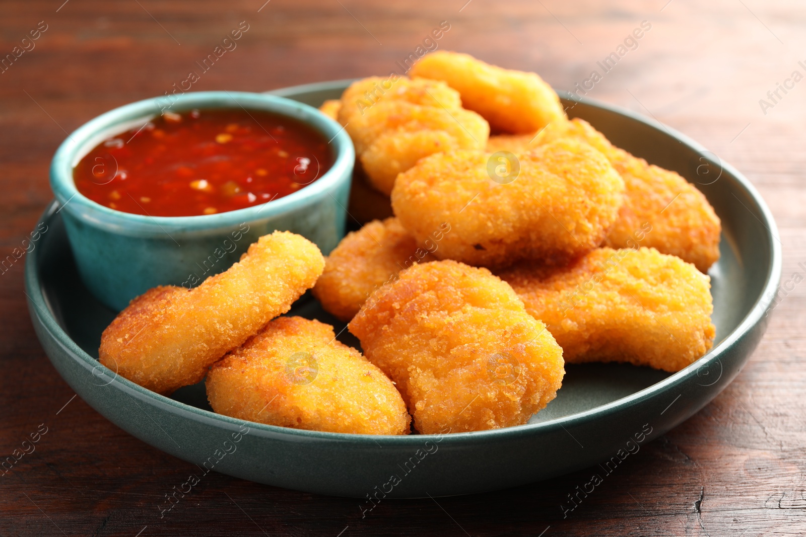 Photo of Plate with hot chili sauce and nuggets on wooden table, closeup