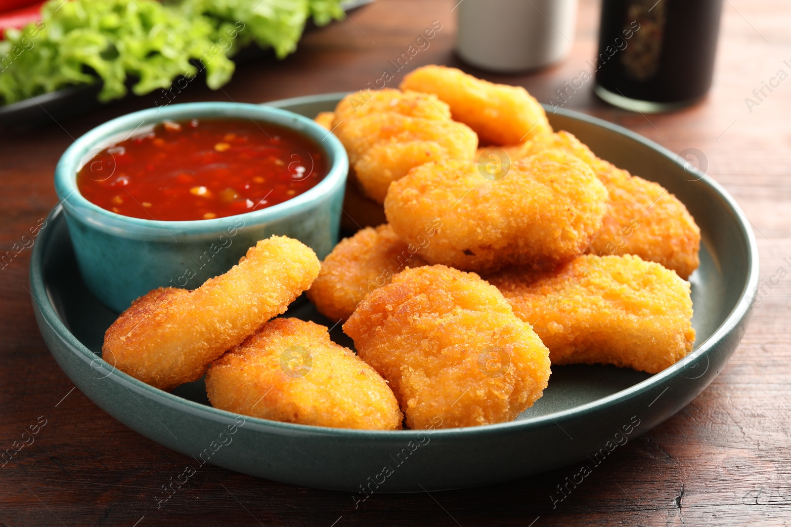 Photo of Plate with hot chili sauce and nuggets on wooden table, closeup