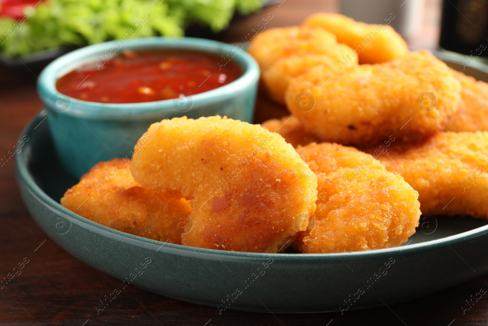 Photo of Plate with hot chili sauce and nuggets on wooden table, closeup