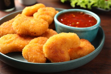 Photo of Plate with hot chili sauce and nuggets on wooden table, closeup