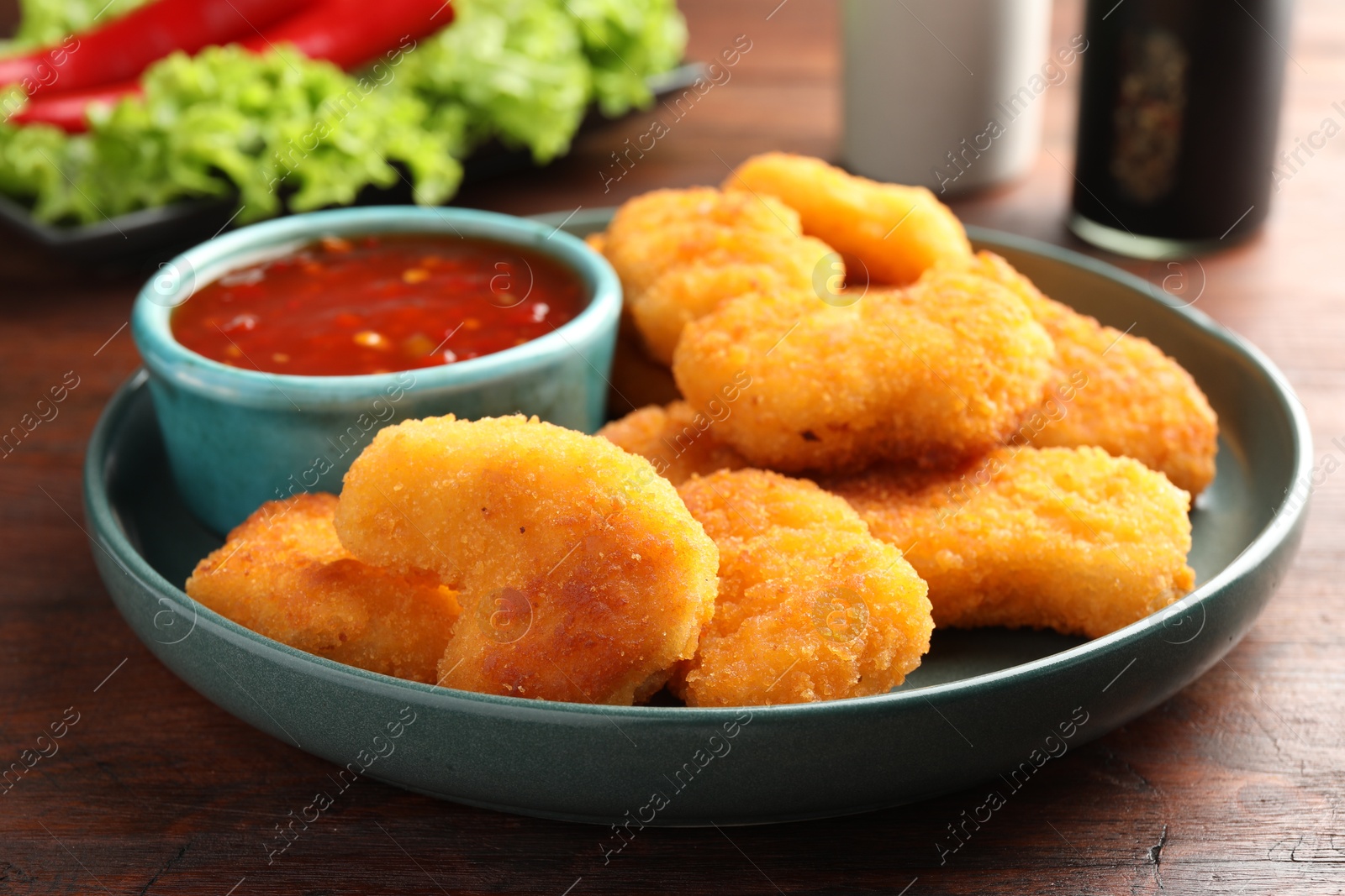 Photo of Plate with hot chili sauce and nuggets on wooden table, closeup