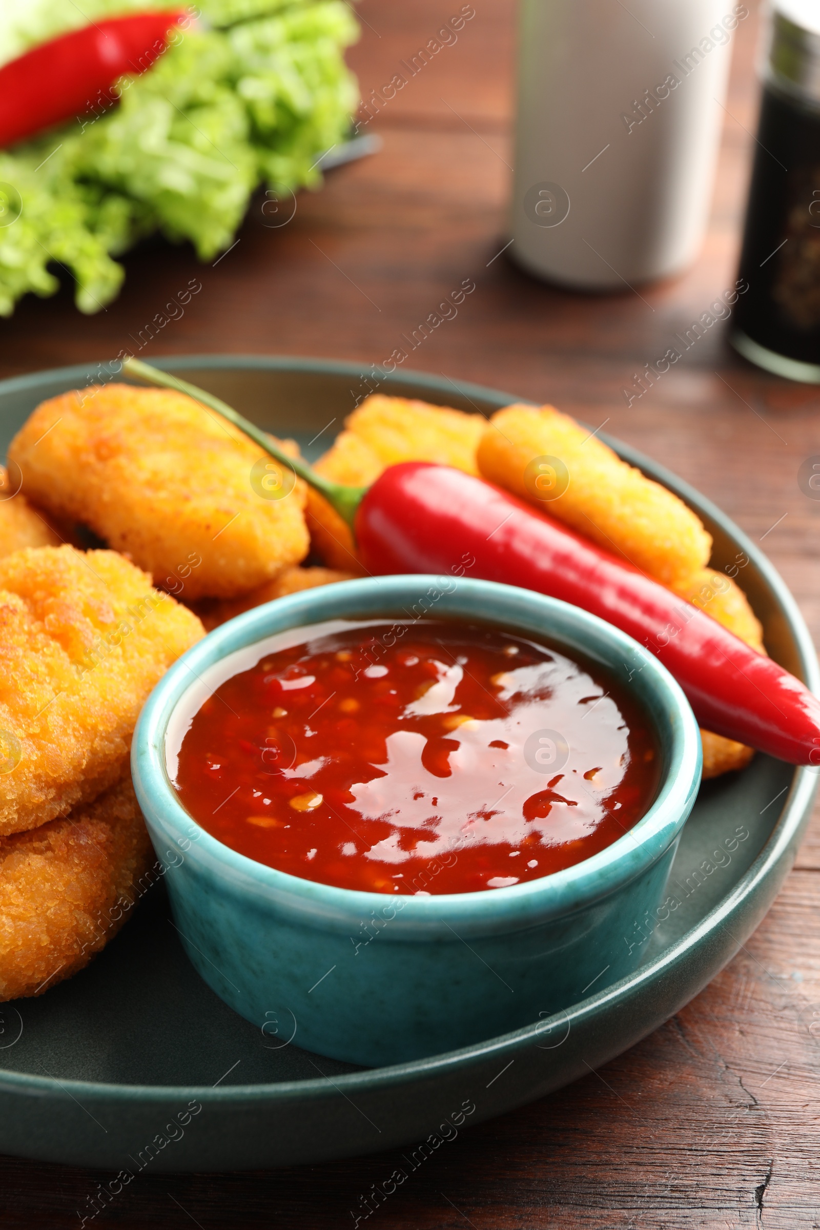 Photo of Plate with hot chili sauce and nuggets on wooden table, closeup