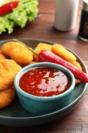 Photo of Plate with hot chili sauce and nuggets on wooden table, closeup