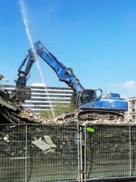 Demolition of building with excavator under blue sky