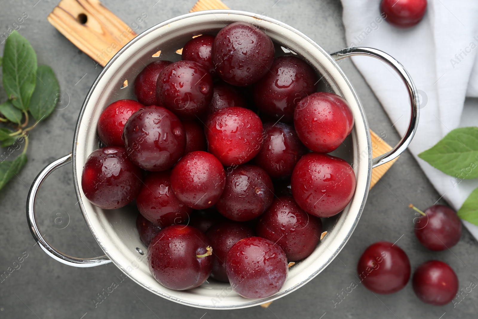 Photo of Tasty ripe plums in colander on grey table, flat lay