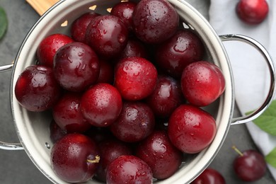 Photo of Tasty ripe plums in colander on grey table, flat lay