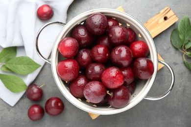 Photo of Tasty ripe plums in colander on grey table, flat lay