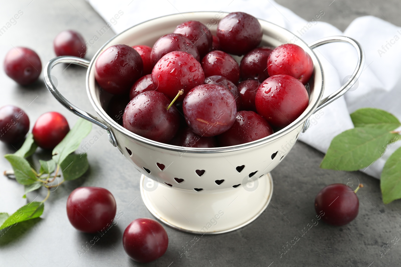 Photo of Tasty ripe plums in colander on grey table, closeup