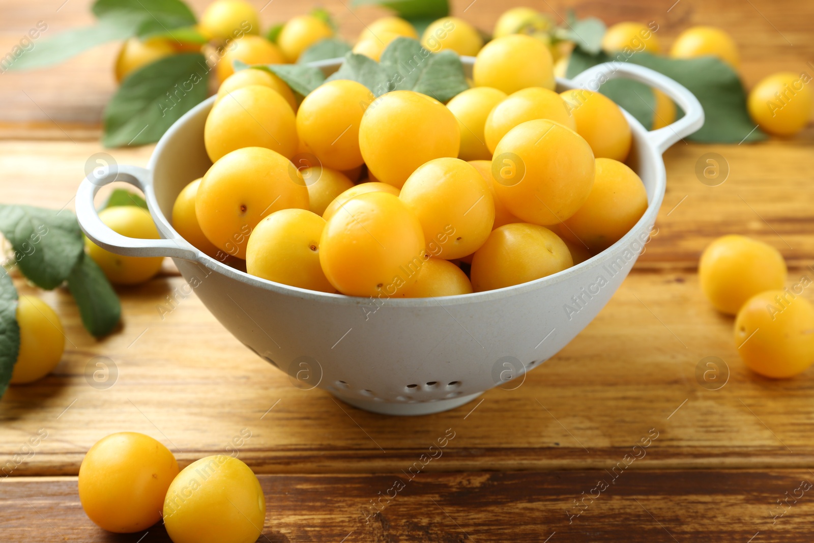 Photo of Tasty ripe plums and leaves in colander on wooden table, closeup