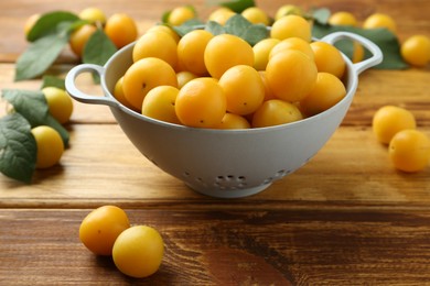 Photo of Tasty ripe plums and leaves in colander on wooden table, closeup