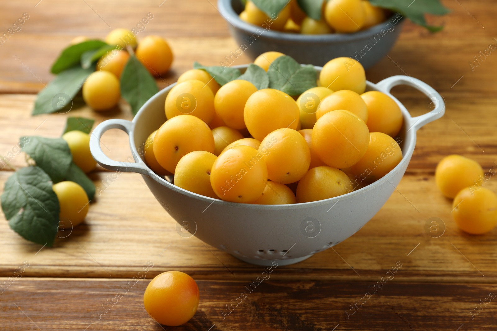 Photo of Tasty ripe plums and leaves in colander on wooden table, closeup