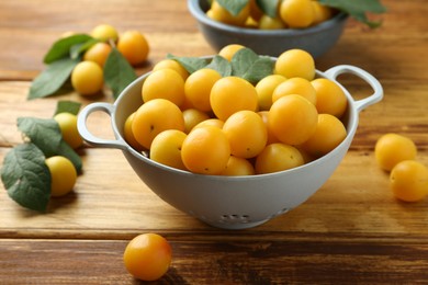 Photo of Tasty ripe plums and leaves in colander on wooden table, closeup