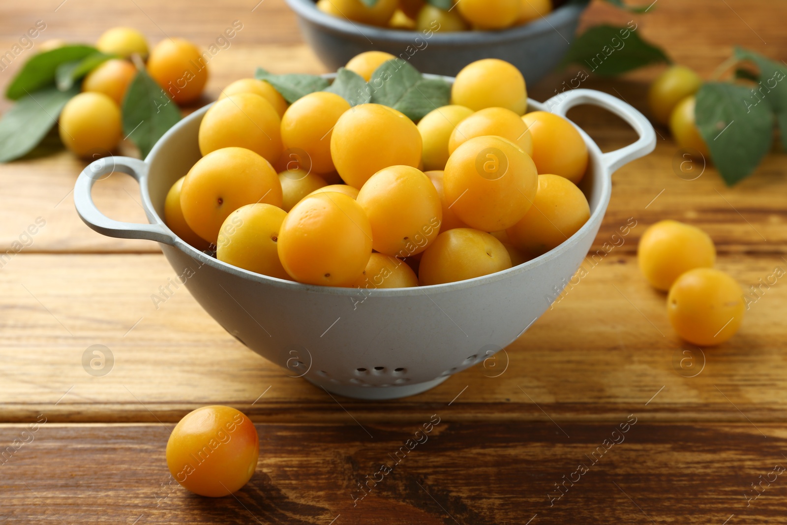 Photo of Tasty ripe plums and leaves in colander on wooden table, closeup