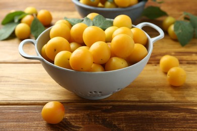 Photo of Tasty ripe plums and leaves in colander on wooden table, closeup